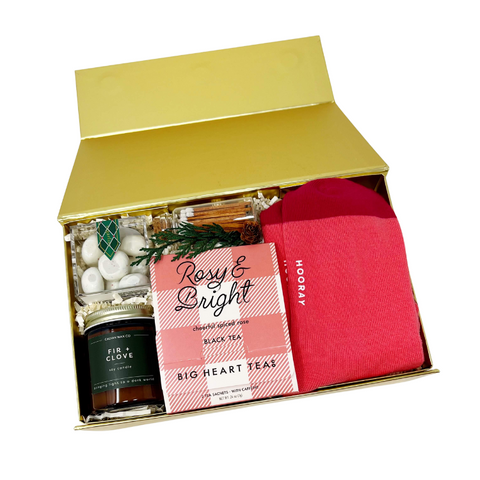 Holiday gift box with bright pink crew socks, spiced black tea sachets, matches, fir & clove candle and peppermint bark cookie bites