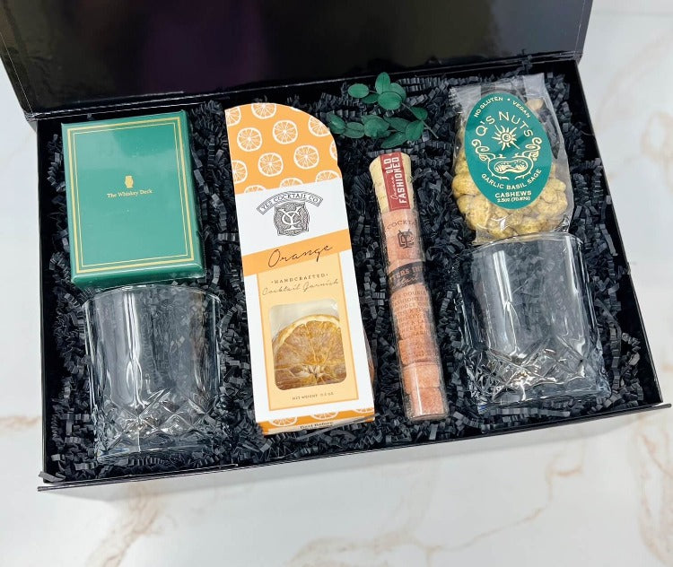 old fashioned gift box with crystal glasses, dried oranges, old fashioned cocktail cubes, a whiskey themed deck of playing cards and roasted herbed cashews