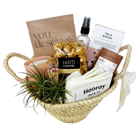 Treat Yourself Gift Basket with self care items like face mask, lotion, tea, chocolate, cozy wool socks, a candle, matches and popcorn