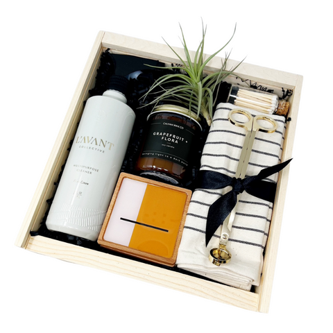 Housewarming or closing gift box with tea towel, candle, multipurpose spray, candle wick trimmer, matches, set of abstract resin coasters and a small air plant.