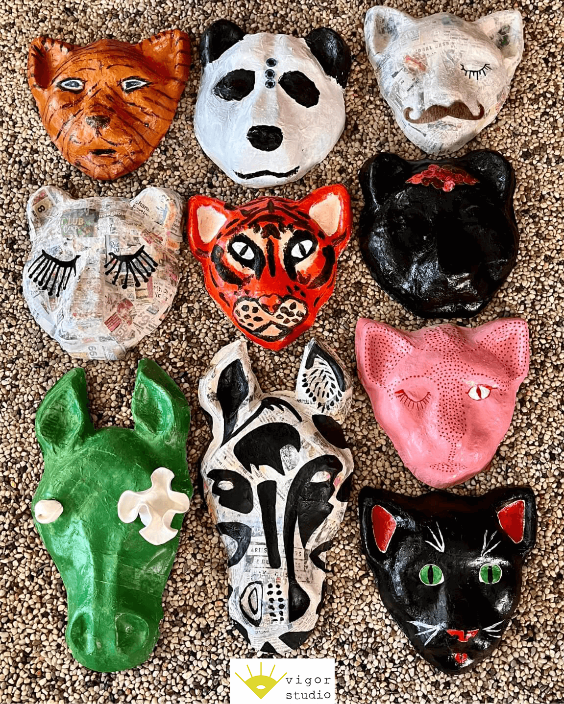 Animal masks made from paper-maché are lined up on the floor. They are a variety of zebras, bears, and tigers painted brightly.